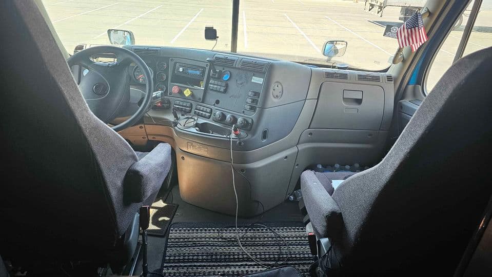 Commercial truck cab interior showing dashboard gauges, steering wheel, and mirrors to inspect